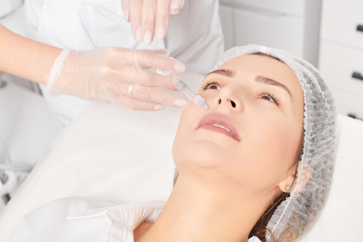 Cosmetologist makes rejuvenation injection in woman face skin, anti aging revitalization cosmetic procedure in beauty salon. Beautician hands in gloves makes facial acid injection treatment